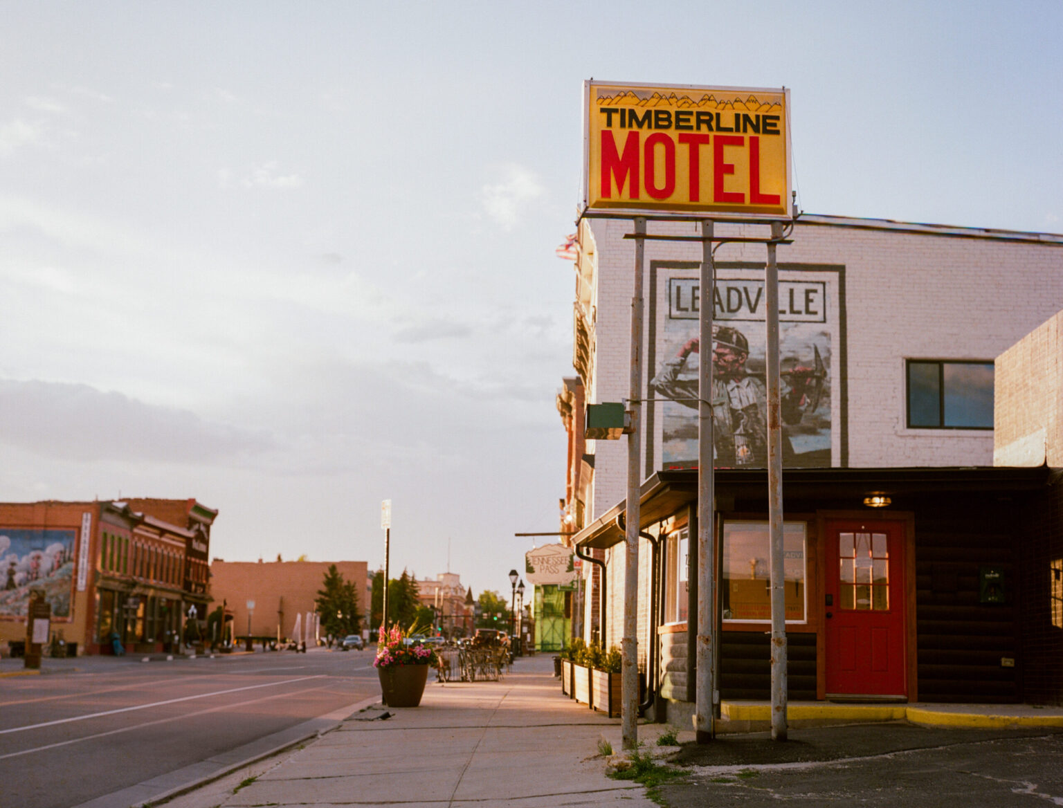 Harrison Avenue in downtown Leadville at sunset, with The Timberline's motel sign and Leadville mural on the right