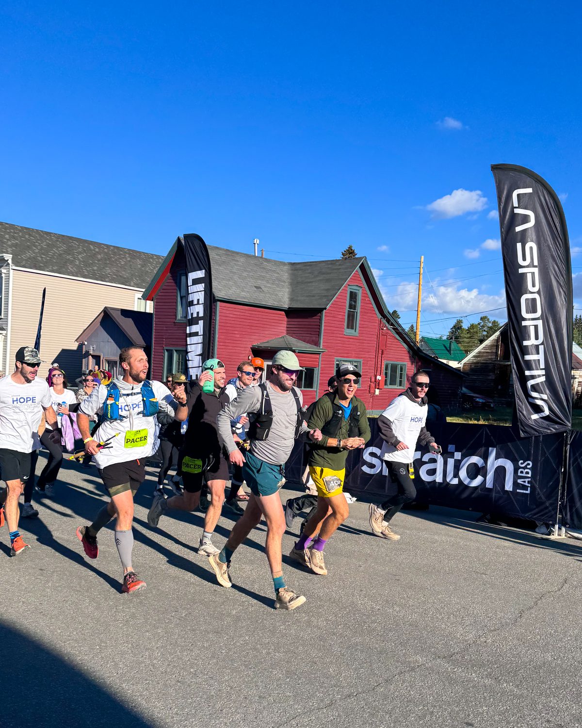 Pacers and crew running a Leadville Trail 100 finisher down Harrison Avenue past a historic red house