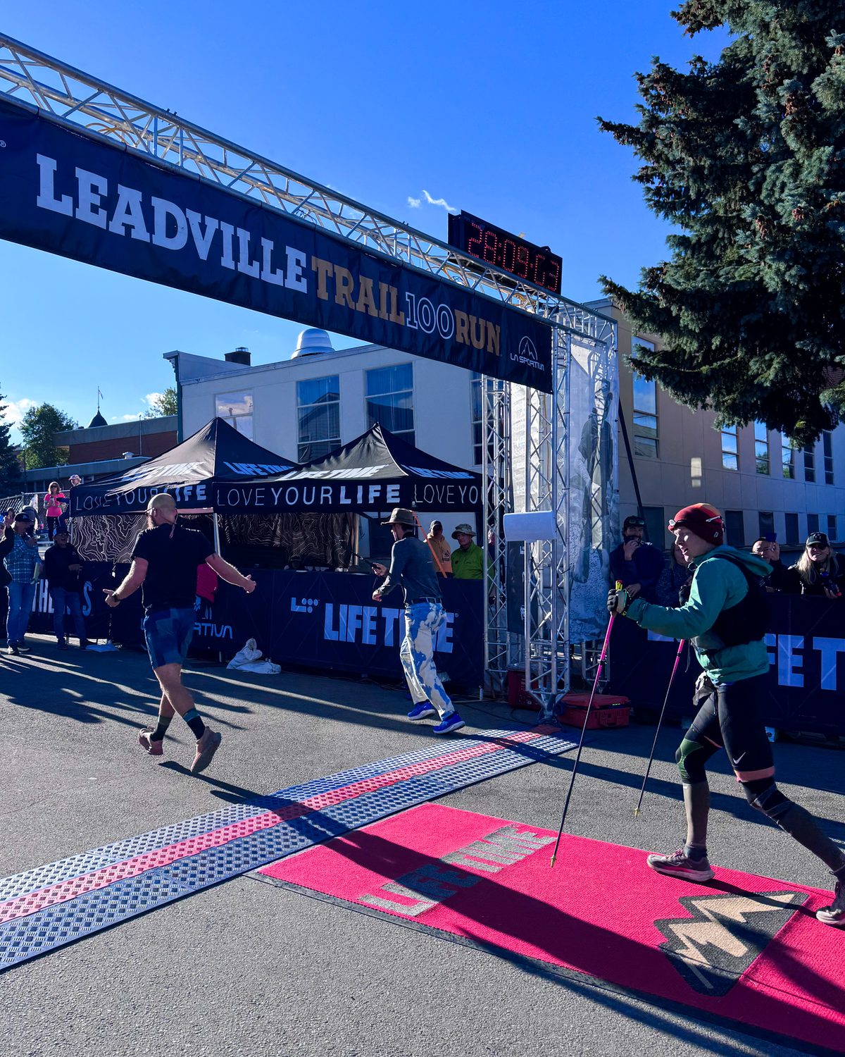 A runner with trekking poles crossing the Leadville Trail 100 Run finish line