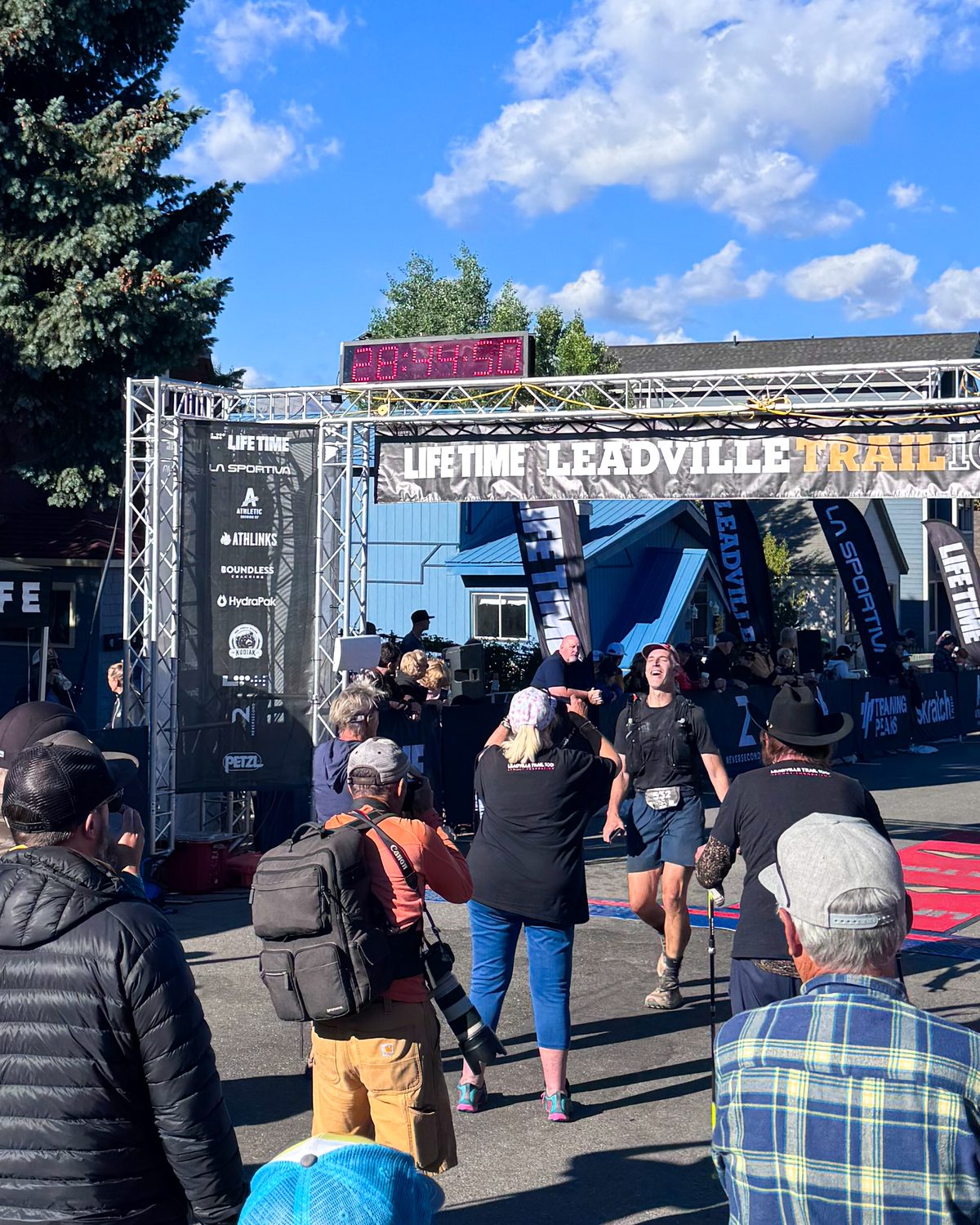 A smiling Leadville Trail 100 Run finisher coming through the arch beneath the race clock