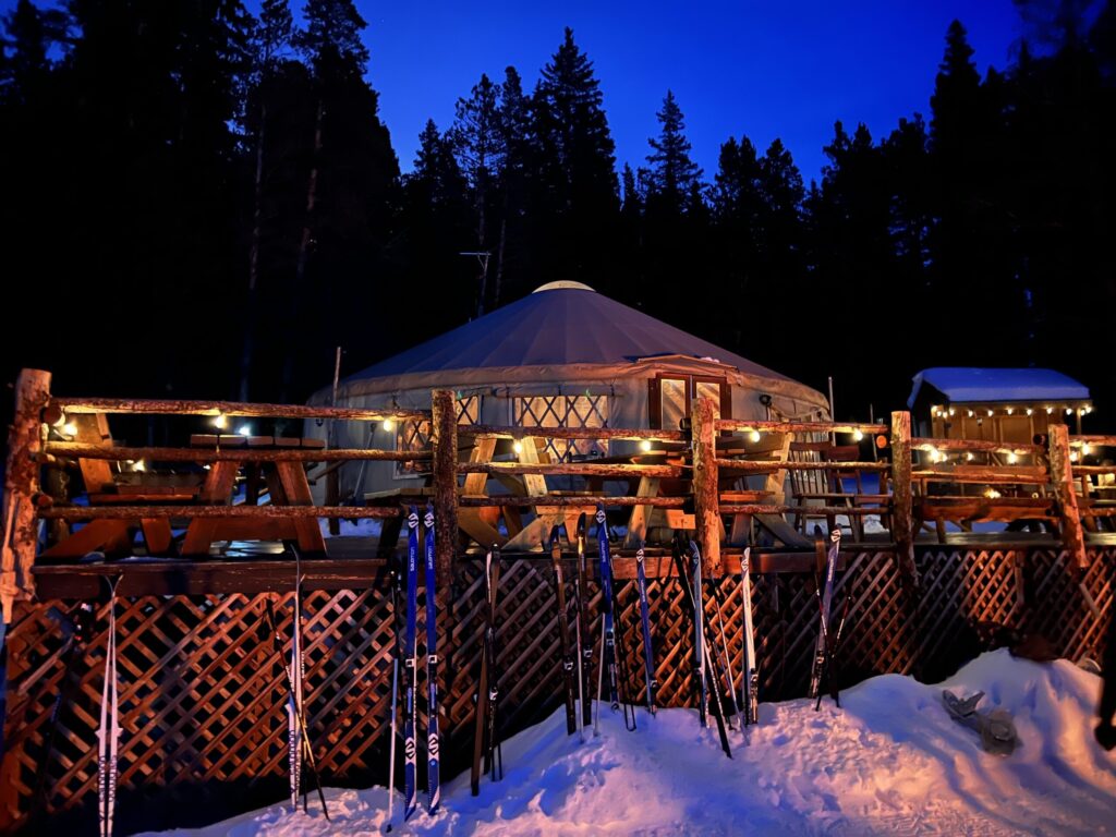 The Tennessee Pass Cookhouse yurt lit up at dusk, with cross-country skis lined up along the snowy deck